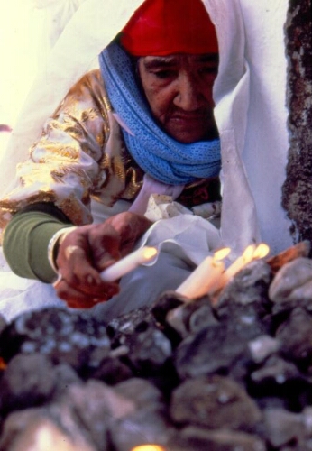 Vieille femme en habit traditionnel mettant des bougies dans la crypte de la synagogue de la Ghriba